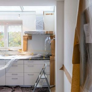 A kitchen under renovation with white cabinets covered in plastic and brown paper